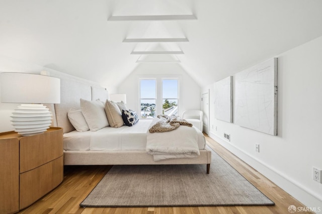 bedroom featuring visible vents, baseboards, lofted ceiling, and wood finished floors
