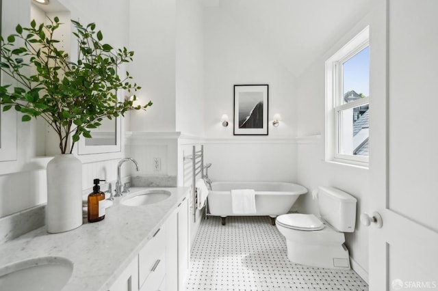 bathroom featuring double vanity, wainscoting, a freestanding tub, toilet, and a sink