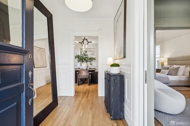 hall with light wood-style floors, crown molding, and a decorative wall