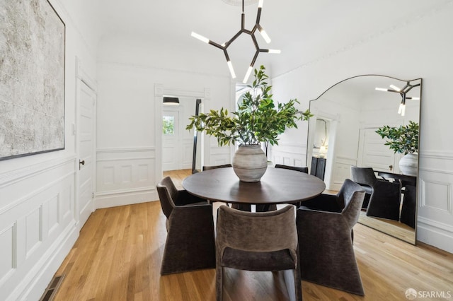 dining area featuring a high ceiling, a decorative wall, light wood finished floors, and a chandelier