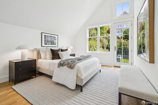 bedroom with light wood-style floors, lofted ceiling, and access to exterior