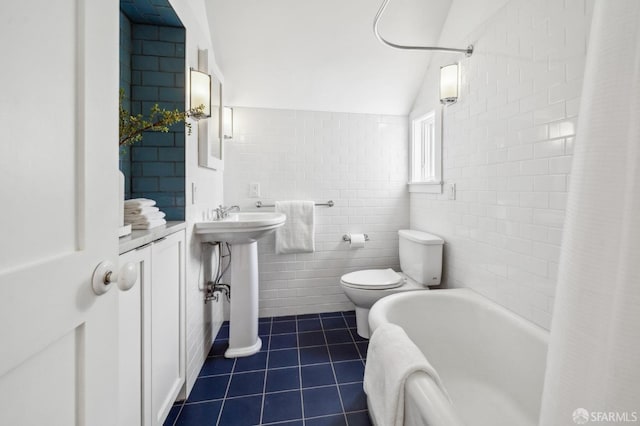 bathroom with tile patterned flooring, toilet, tile walls, a sink, and vaulted ceiling