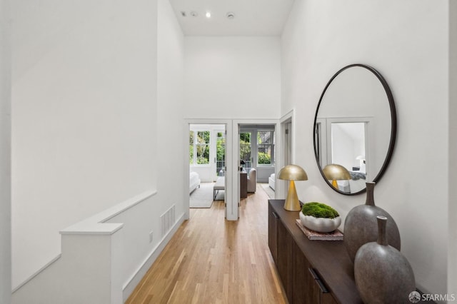 corridor featuring visible vents, a towering ceiling, light wood-style floors, baseboards, and french doors