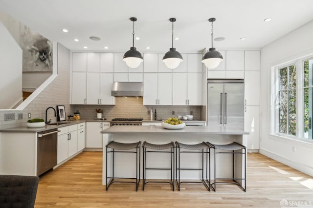 kitchen featuring a sink, a breakfast bar area, stainless steel appliances, decorative backsplash, and under cabinet range hood