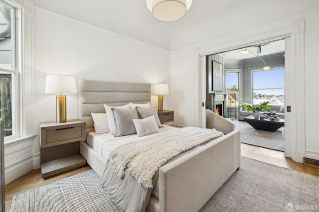 bedroom with a lit fireplace, wood finished floors, and access to exterior