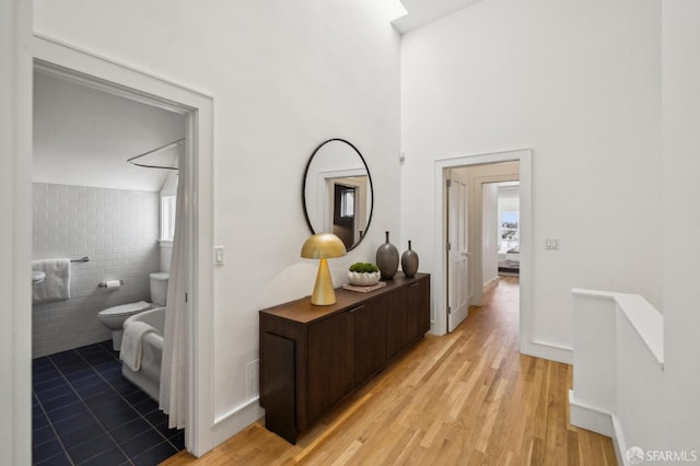 hall featuring light wood-style floors and a towering ceiling