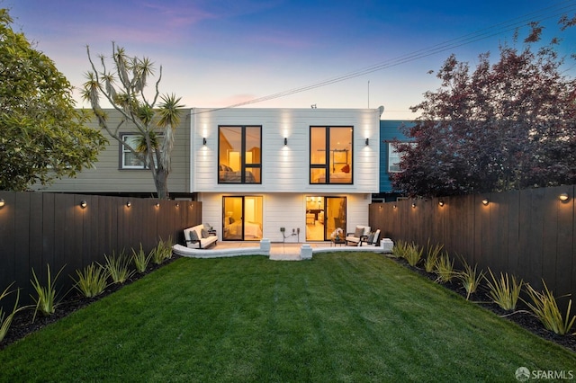 back house at dusk featuring a patio and a lawn