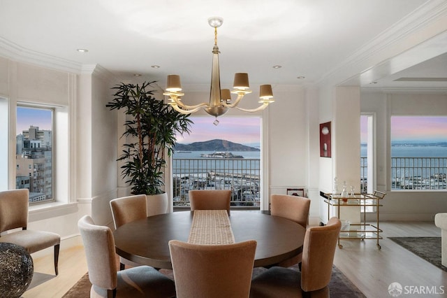 dining room with a healthy amount of sunlight, a water view, ornamental molding, and hardwood / wood-style flooring