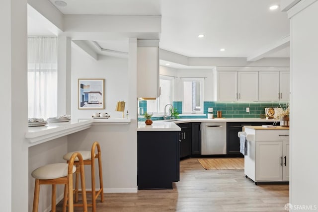 kitchen with tasteful backsplash, stainless steel dishwasher, light countertops, a sink, and light wood finished floors