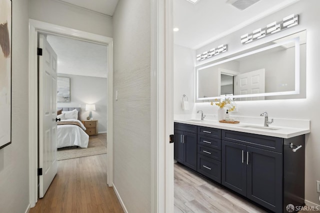 ensuite bathroom with double vanity, ensuite bath, a sink, and wood finished floors
