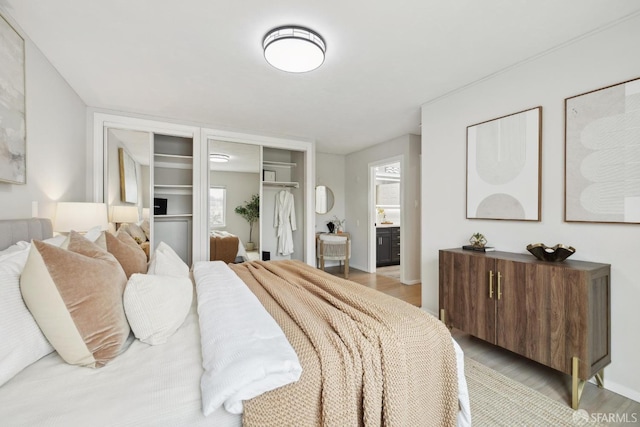 bedroom featuring light wood-style floors, baseboards, and ensuite bath