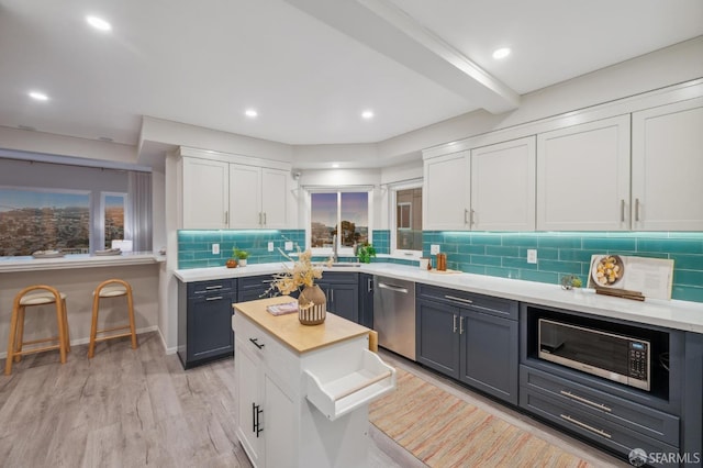 kitchen with stainless steel dishwasher, light wood-type flooring, white cabinetry, tasteful backsplash, and a sink