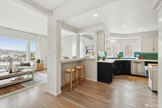 kitchen featuring stainless steel dishwasher, light countertops, tasteful backsplash, dark cabinets, and light wood finished floors
