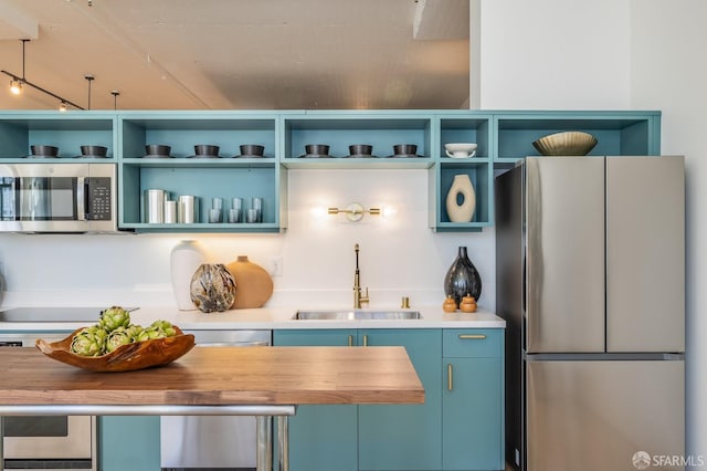 kitchen with stainless steel appliances, blue cabinets, butcher block counters, and sink