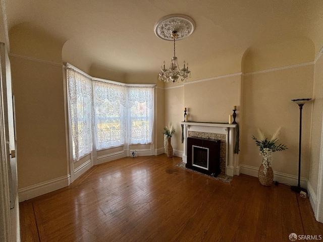 unfurnished living room featuring a notable chandelier, wood finished floors, baseboards, and a premium fireplace