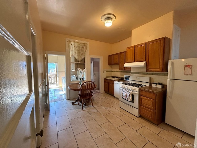 kitchen featuring brown cabinets, under cabinet range hood, a sink, tasteful backsplash, and white appliances