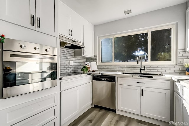 kitchen with a sink, stainless steel appliances, light wood-type flooring, under cabinet range hood, and backsplash