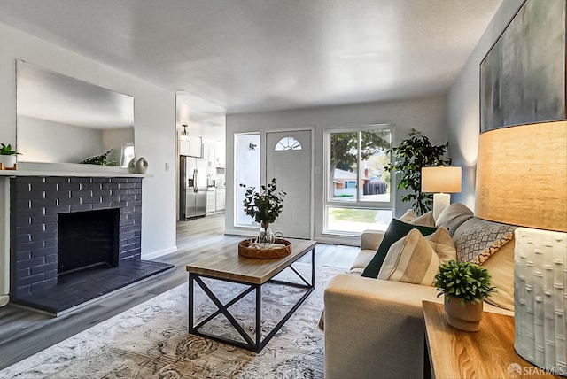 living room with a brick fireplace, baseboards, and wood finished floors