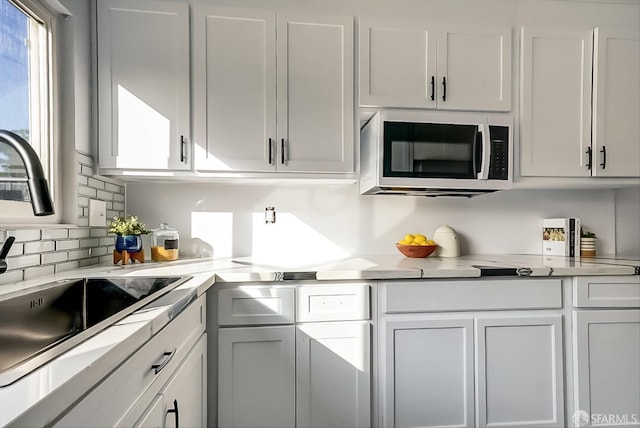 kitchen with light countertops, stainless steel microwave, a sink, and white cabinets