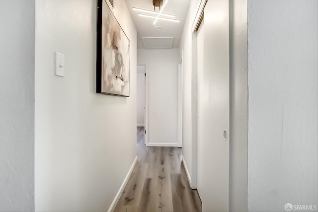 hall featuring light wood finished floors, attic access, and baseboards