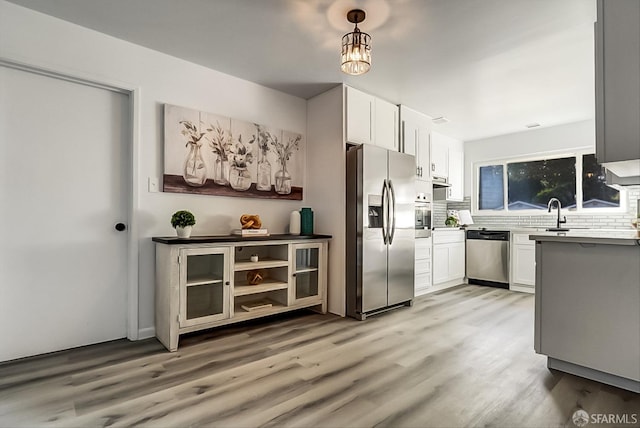 kitchen with appliances with stainless steel finishes, backsplash, a sink, and light wood-style flooring