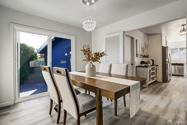 dining space featuring visible vents, light wood-style flooring, and an inviting chandelier