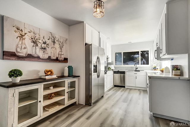 kitchen featuring decorative backsplash, stainless steel appliances, light wood-style floors, white cabinetry, and a sink