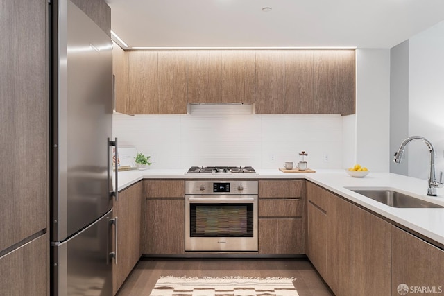 kitchen featuring light wood-type flooring, a sink, appliances with stainless steel finishes, light countertops, and decorative backsplash