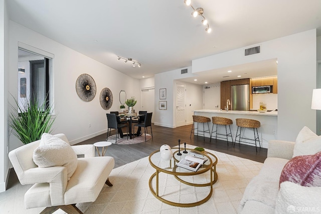 living room featuring track lighting, dark wood-style floors, visible vents, and baseboards