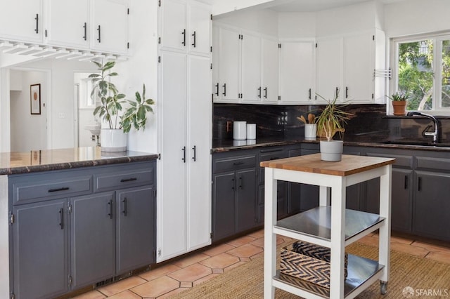 kitchen featuring light tile patterned floors, dark stone counters, a sink, white cabinets, and backsplash