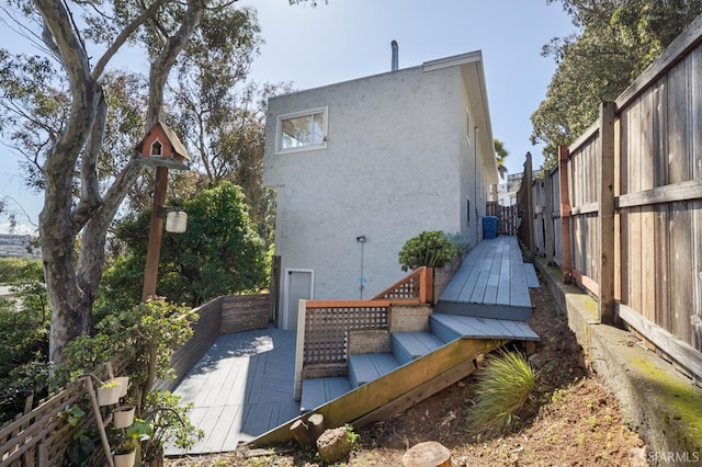 back of house with stucco siding, a deck, and fence