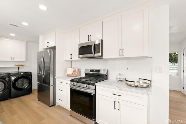 kitchen with light stone counters, light wood-style flooring, separate washer and dryer, white cabinets, and appliances with stainless steel finishes