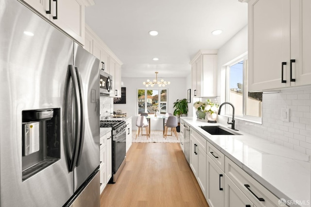 kitchen with light stone counters, a sink, white cabinets, appliances with stainless steel finishes, and light wood finished floors