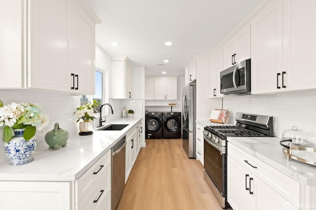 kitchen with stainless steel appliances, white cabinets, a sink, and separate washer and dryer