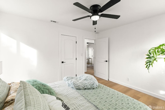 bedroom featuring a ceiling fan, wood finished floors, visible vents, and baseboards