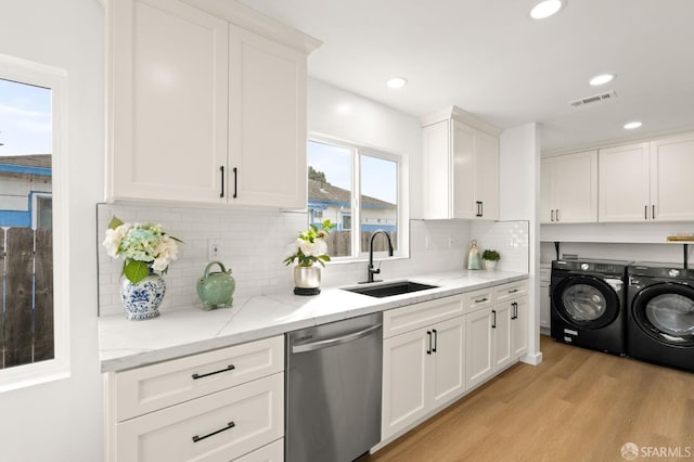 kitchen featuring visible vents, stainless steel dishwasher, white cabinets, a sink, and washer and dryer