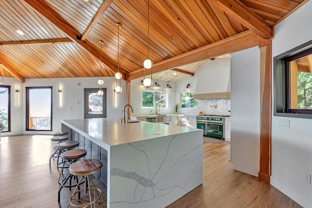 kitchen featuring stainless steel range, vaulted ceiling with beams, backsplash, a large island with sink, and pendant lighting