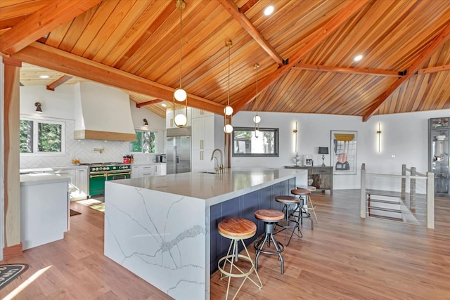 kitchen with white cabinetry, premium appliances, backsplash, decorative light fixtures, and custom exhaust hood