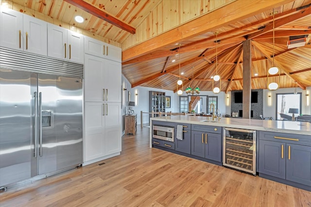 kitchen with beverage cooler, pendant lighting, built in appliances, beam ceiling, and white cabinets