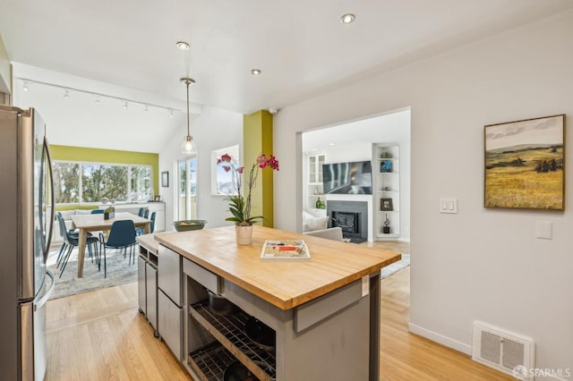 kitchen with butcher block countertops, stainless steel refrigerator, a kitchen island, decorative light fixtures, and vaulted ceiling