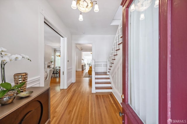 foyer entrance with stairway, an inviting chandelier, a decorative wall, and light wood-style floors