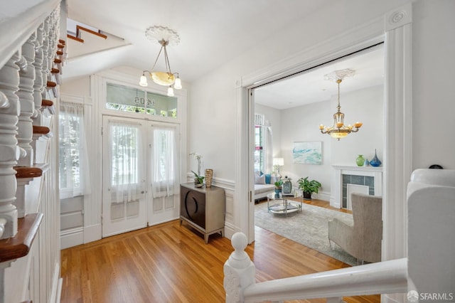 foyer featuring stairway, wood finished floors, french doors, a tiled fireplace, and a chandelier