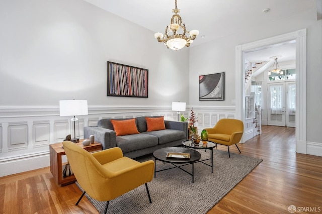 living area featuring wood finished floors, french doors, wainscoting, a decorative wall, and a chandelier