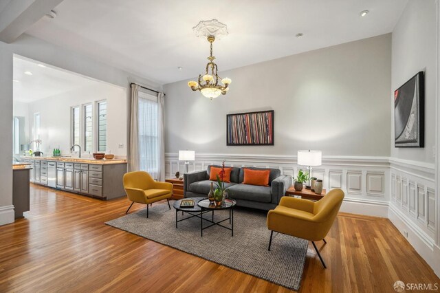 living room with a chandelier, a wainscoted wall, a decorative wall, and wood finished floors