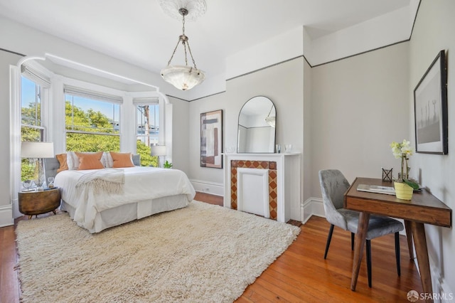 bedroom featuring baseboards, wood finished floors, and a tiled fireplace