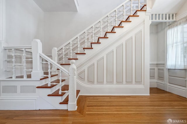 stairs featuring a decorative wall, wainscoting, and wood finished floors