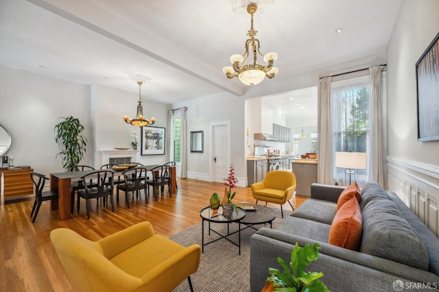 living room with beamed ceiling, baseboards, a notable chandelier, and light wood finished floors