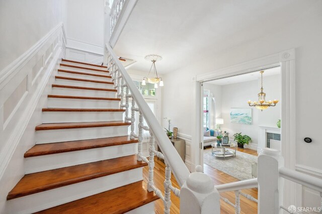 stairway with a tiled fireplace, an inviting chandelier, a decorative wall, and wood finished floors