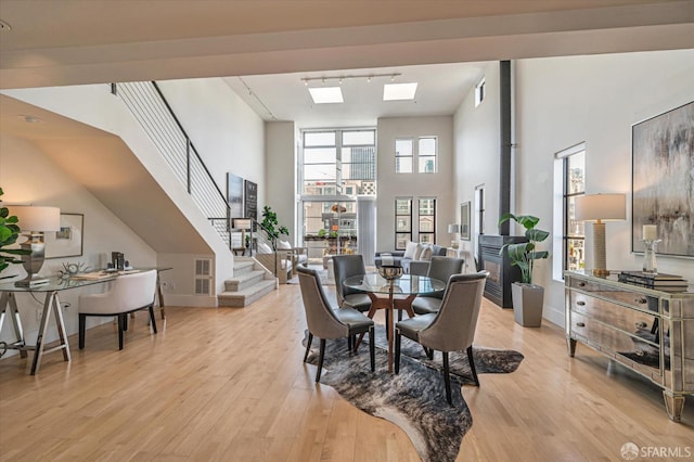 dining space with a towering ceiling, a skylight, a wood stove, and light wood-type flooring