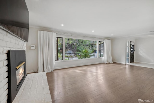 unfurnished living room with recessed lighting, wood finished floors, baseboards, a glass covered fireplace, and crown molding